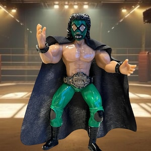 May include: Action figure of a wrestler named Espectro, wearing a green mask, green tights, and black boots. The figure has a black cape and a championship belt. The figure is posed with arms outstretched.