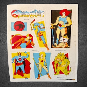 May include: A rectangular sticker sheet featuring ThunderCats characters and logos. The sheet includes illustrations of Lion-O with the Sword of Omens, Snarf, Panthro, Cheetara, Tygra, and a green reptilian creature, all set against colorful geometric backgrounds.