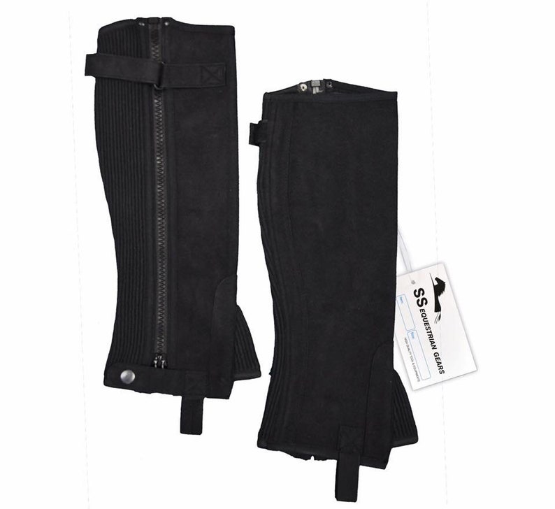 May include: A pair of black suede riding chaps with a zipper up the front and a strap with a buckle at the top. The chaps have a ribbed design and a button at the bottom.