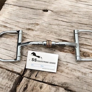 May include: A polished metal horse bit with D-shaped rings on each end and a central joint with copper-colored accents. A white card with the text "SS Equestrian Gears" is also present.