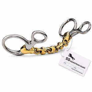 May include: A metal horse bit featuring silver-coloured rings and a gold-coloured jointed mouthpiece. A white rectangular tag is attached, displaying the text SS EQUESTRIAN GEARS, a horse silhouette, and blank fields for date and order information.