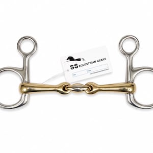 May include: A silver and brass coloured metal horse bit with a central jointed mouthpiece and two large circular rings on each side. A white rectangular tag is attached, featuring a black horse logo and the text SS EQUESTRIAN GEARS.