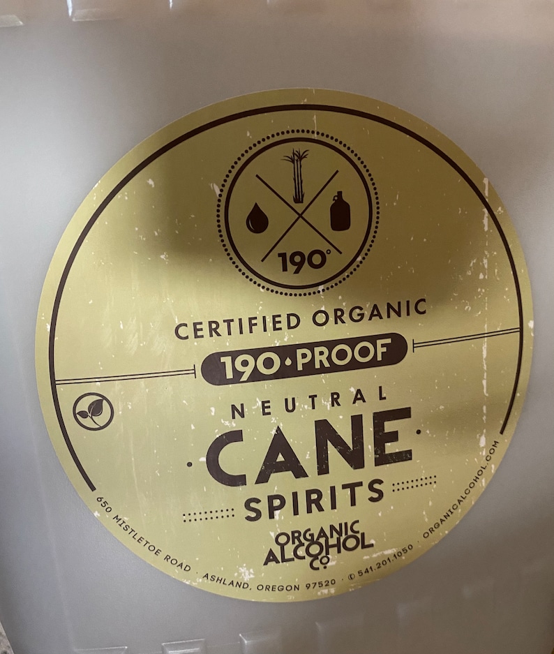 Puede incluir: Una etiqueta circular dorada y marr&oacute;n con el texto "Certified Organic 190-Proof Neutral Cane Spirits Organic Alcohol Co. 650 Mistletoe Road Ashland, Oregon 97520 (541) 201-1050 OrganicAlcohol.com" y un logotipo de un tallo de ca&ntilde;a de az&uacute;car, una gota de l&iacute;quido y una botella con el n&uacute;mero 190 grados.
