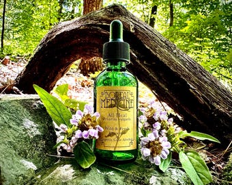 May include: A green glass bottle with a dropper top, labeled "Boreal Medicine" and "All Heal Prunella vulgaris Wild & Fresh Extract 1oz Organic Cane Alcohol". The bottle is sitting on a rock with purple flowers.