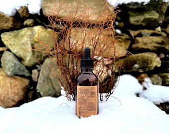 May include: A brown glass bottle with a black dropper cap, labeled "BOREAL MEDICINE." The label includes text about Japanese Knotweed and other ingredients. The bottle is set in snow, with a backdrop of a stone wall and dried, reddish-brown branches.