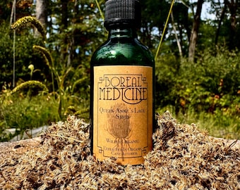 Può includere: Una bottiglia di vetro verde con un contagocce nero è etichettata "Boreal Medicine". L'etichetta beige ha testo marrone e una grafica di una testa di seme. La bottiglia è appoggiata su un letto di semi secchi, con uno sfondo sfocato di foresta.