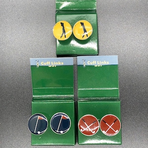 May include: Two sets of golf-themed cufflinks. The first set features a yellow background with a black silhouette of a golfer swinging a club. The second set features a blue background with a pair of crossed golf clubs.