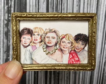 May include: A framed watercolor painting of five women with blonde hair. The women are smiling and looking at the camera. The painting is in a gold frame.