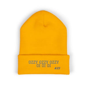 May include: Mustard yellow beanie with the text "OZZY OI OI OI" and the number "#89" in navy blue. The beanie is a knit cap, perfect for cold weather. The hat is a solid color with a folded brim.