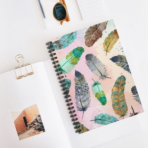 May include: A pink spiral notebook with a watercolor pattern of colorful feathers. The feathers are in shades of blue, green, brown, and gray.