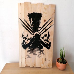 Peut inclure: Une pancarte en bois avec une silhouette noire de Wolverine, un personnage de bande dessinée populaire, avec ses griffes déployées. La pancarte est faite de bois de récupération et a un aspect rustique.