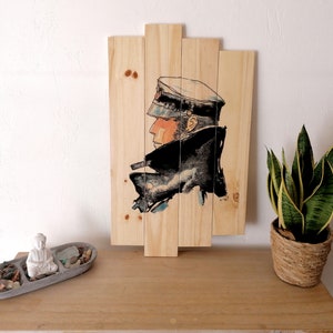 Könnte beinhalten: Ein Wandbild aus Holz mit einer Schwarzweißillustration einer Person mit Hut und Mantel. Die Illustration ist auf eine Reihe von Holzbrettern gedruckt.