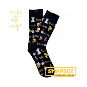 Puede incluir: Un par de calcetines negros con temática de café. Los calcetines presentan una variedad de imágenes relacionadas con el café, incluyendo tazas de café, granos de café y cafeteras. Los calcetines también tienen el texto "latte", "café", "brew", "java" y "espresso" impreso en ellos. Los calcetines están hechos por Snapsox, una empresa que fabrica calcetines con broches para evitar que se pierdan en la lavandería.