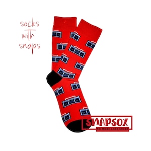 May include: A pair of red socks with a repeating pattern of blue and black boomboxes. The socks have black heels and toes. The text "socks with snaps" is in the upper left corner. The brand name "SNAPSox" is in the lower right corner.