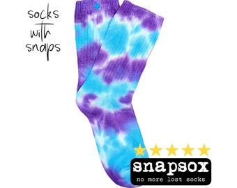 Peut inclure: Une paire de chaussettes tie-dye dans les tons de violet et de bleu turquoise. Les chaussettes ont une fermeture à bouton-pression en haut et le texte "socks with snaps" est écrit en police script. La marque "snapsox" est affichée avec une note de cinq étoiles.