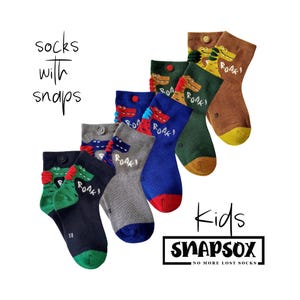 May include: A collection of colorful kids' socks with snap closures, featuring cartoon dinosaur designs and the word "ROAR!". The socks come in various colors, including blue, green, gray, and brown, with the brand name "SNAPSOX".