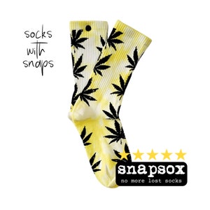 May include: A pair of yellow and white socks with black cannabis leaf patterns. The socks have a tie-dye effect and feature the text "socks with snaps" and the brand name "snapsox" with the tagline "no more lost socks".