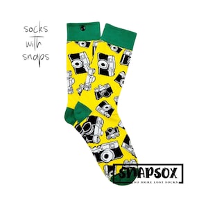 May include: A pair of yellow socks with a green cuff and a black snap closure. The socks feature a repeated pattern of black and white cameras. The text "Snapsox" and "No More Lost Socks" is printed on the bottom of the socks.