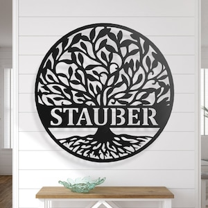 May include: A black metal family tree wall art piece. The circular tree design features the family name "STAUBER" cut out at the base. The tree has detailed leaves and roots, suitable for indoor or outdoor display.