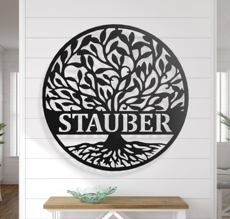 May include: A black metal family tree wall art piece. The circular tree design features the family name "STAUBER" cut out at the base. The tree has detailed leaves and roots, suitable for indoor or outdoor display.