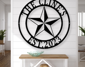 May include: Black metal wall art with a star design inside a circular frame. The text "THE CLINE'S EST 2023" is displayed around the star. The artwork is mounted on a white wall above a wooden console table.