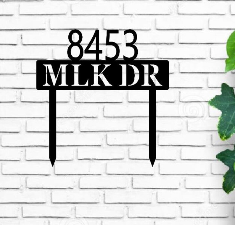 May include: Black metal house number sign with the numbers 8453 and the street name MLK DR. The sign is attached to two metal stakes.