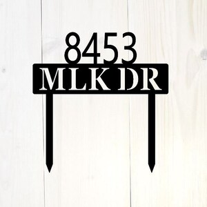May include: Black metal house number sign with the number 8453 and the name MLKDR in white lettering.