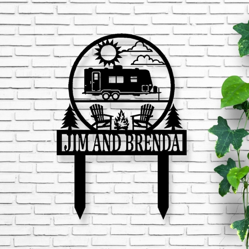 May include: Black metal camping-themed yard stake featuring a camper, sun, clouds, Adirondack chairs, and a campfire within a circle. The stake includes the names "JIM AND BRENDA" in a rectangular banner, perfect for outdoor decor.