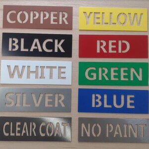 May include: A collection of rectangular metal stencils in various colors, each displaying a different color name in capital letters. Colors include copper, yellow, black, red, white, green, silver, blue, clear coat, and no paint.
