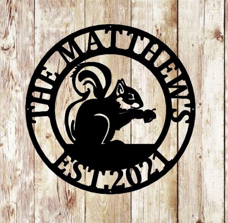 May include: Black metal sign with the text "The Matthews Est. 2021" in a circle. A silhouette of a squirrel holding a nut is in the centre of the circle.
