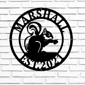 May include: Black metal circular sign with the words "MARSHALL EST 2021" around the edge. A silhouette of a squirrel holding a nut is in the centre.