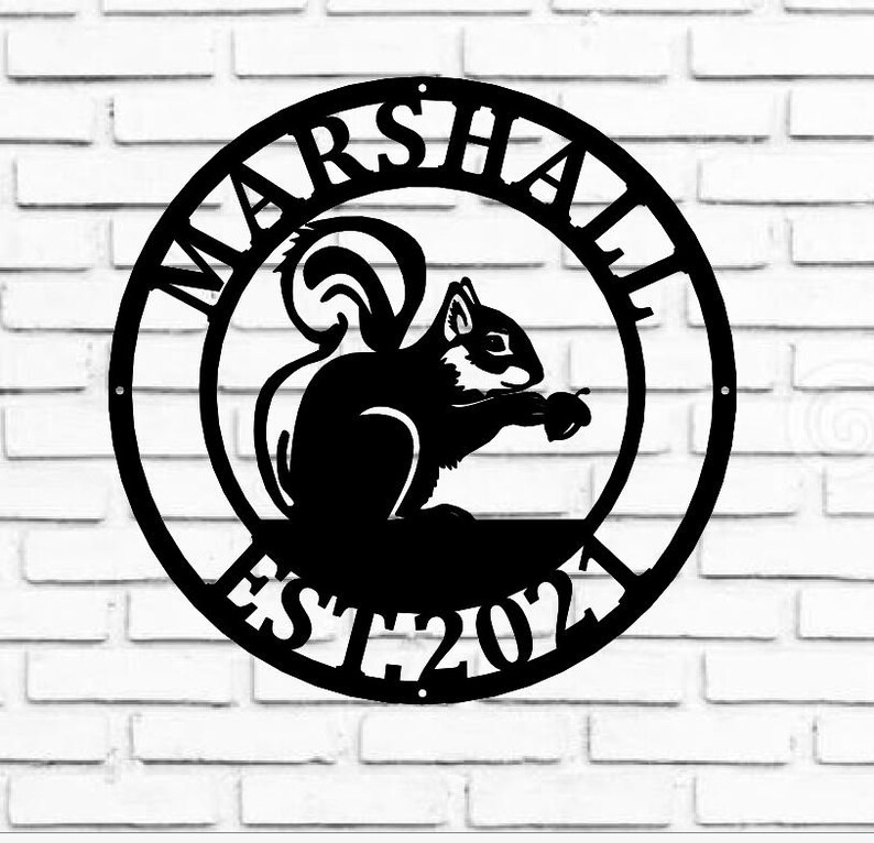 May include: Black metal circular sign with the words "MARSHALL EST 2021" around the edge. A silhouette of a squirrel holding a nut is in the centre.