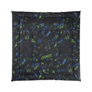 May include: Black comforter with a gamer-themed pattern. The design includes keyboards, controllers, headphones, and lightning bolts in blue and green. Text includes "GAME ON", "GAMER", and "LEVEL UP".
