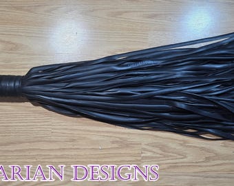 Könnte beinhalten: Schwarzer Lederflogger mit gewickeltem Griff und Metallring. Der Flogger hat viele lange, dünne Lederstränge. Der Text "BARBARIAN DESIGNS" ist unten im Bild zu sehen.