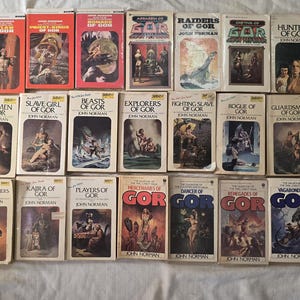 May include: A collection of vintage paperback books from the Gor series by John Norman. The covers feature illustrations with titles like "Raiders of Gor" and "Hunters of Gor." The books are arranged on a white surface.