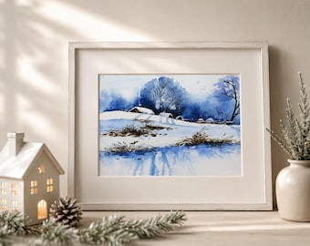 May include: A framed watercolor painting depicting a snowy winter landscape with blue-toned trees, small houses, and a frozen body of water. The artwork is displayed in a light-colored wooden frame, accompanied by a white ceramic house and a vase.