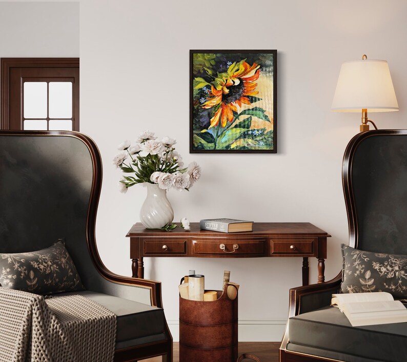 以下が含まれることがあります： オレンジと黄色の花びら、緑の葉、濃い茶色の背景を持つひまわりを描いた額縁付きの絵画。絵画はリビングルームの白い壁に飾られています。