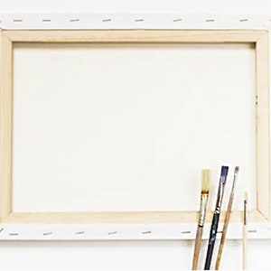 以下が含まれることがあります： 木製のフレームに張られた白いキャンバスは、絵を描く準備ができています。4本の筆がフレームに寄りかかっています。