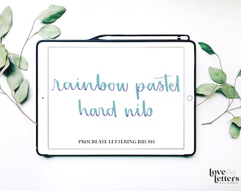 May include: A white tablet screen with the text "rainbow pastel hard nib" in a blue and purple gradient font. The text "PROCREATE LETTERING BRUSH" is below the main text. The tablet is on a white surface with green leaves on either side.