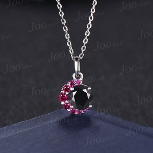 May include: A silver chain necklace with a black gemstone pendant surrounded by a halo of smaller pink gemstones.