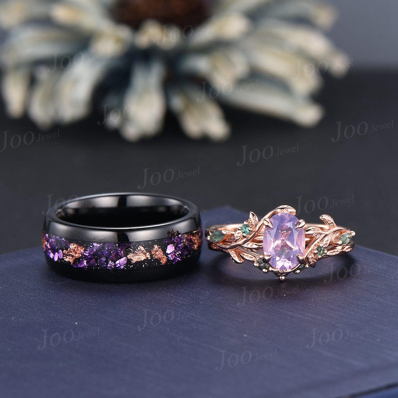Puede incluir: Dos anillos: una banda negra con detalles morados y dorados, y un anillo de oro rosa con una piedra ovalada de color p&uacute;rpura claro y detalles de hojas. Los anillos est&aacute;n sobre un fondo azul oscuro.