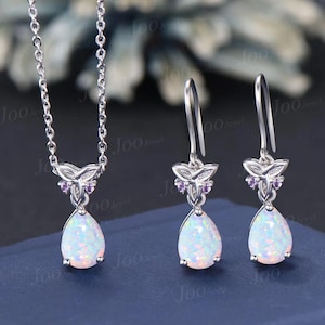 May include: A silver jewellery set comprising a necklace and earrings. The necklace features a pendant with a white opal teardrop and a floral design with purple accents. The earrings have a matching design.