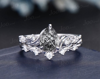May include: A pear-shaped black rutilated quartz engagement ring set with a delicate, vine-like band and smaller diamonds. The ring is set in silver.