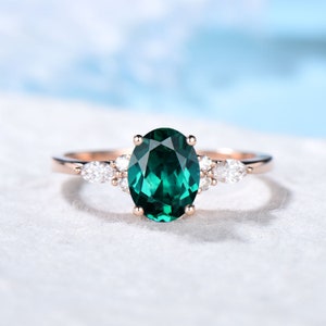Op de afbeelding: Roségouden ring met een ovaal geslepen smaragdgroene edelsteen als middelpunt, geflankeerd door kleinere, heldere edelstenen. De ring heeft een delicate roségouden kleur en de zetting is in klassieke prong-stijl.