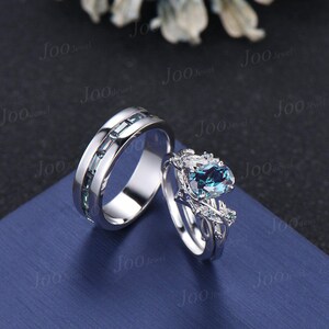 May include: A matching wedding ring set featuring a silver band with rectangular blue-green stones and a silver engagement ring with a large oval blue-green gemstone and smaller accent stones. The rings are displayed on a blue surface.