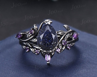 May include: A black ring set with a pear-shaped, dark blue gemstone and small purple gemstones. The ring has a floral design with leaves and vines. The ring is set against a dark blue background. The text "Joo Jewel" is visible in the image.