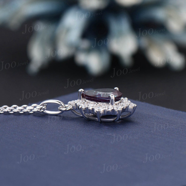 May include: A silver necklace with a pendant featuring a dark purple oval gemstone surrounded by small, clear gemstones. The pendant is set in a silver metal frame. The chain is delicate and also silver.