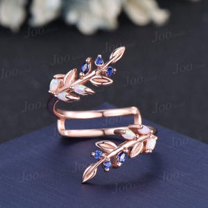 May include: Rose gold ring with a leaf design. The ring features opal and sapphire gemstones. The ring is a double band design with the text "Joo Jewel" in the background.