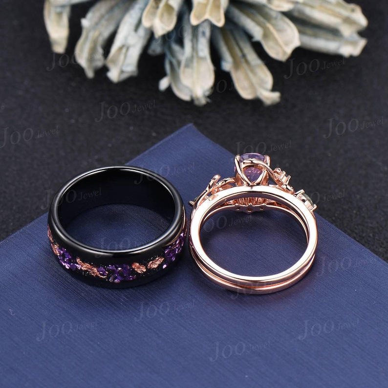 Puede incluir: Dos anillos: una banda negra con piedras preciosas moradas y un anillo de compromiso de oro rosa con una gran piedra preciosa morada. Los anillos se muestran sobre una superficie azul, con un fondo floral borroso.