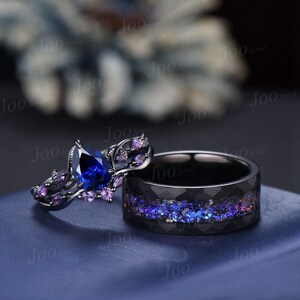 Può includere: Un anello di fidanzamento a forma di pera nero e blu con una fascia nera e una fede nuziale nera abbinata con un design a galassia blu e viola.